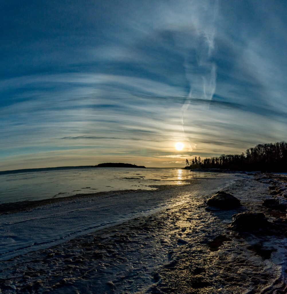 Serene beach at sunset with golden light calm water textured shoreline and wispy clouds sky Wallpaper