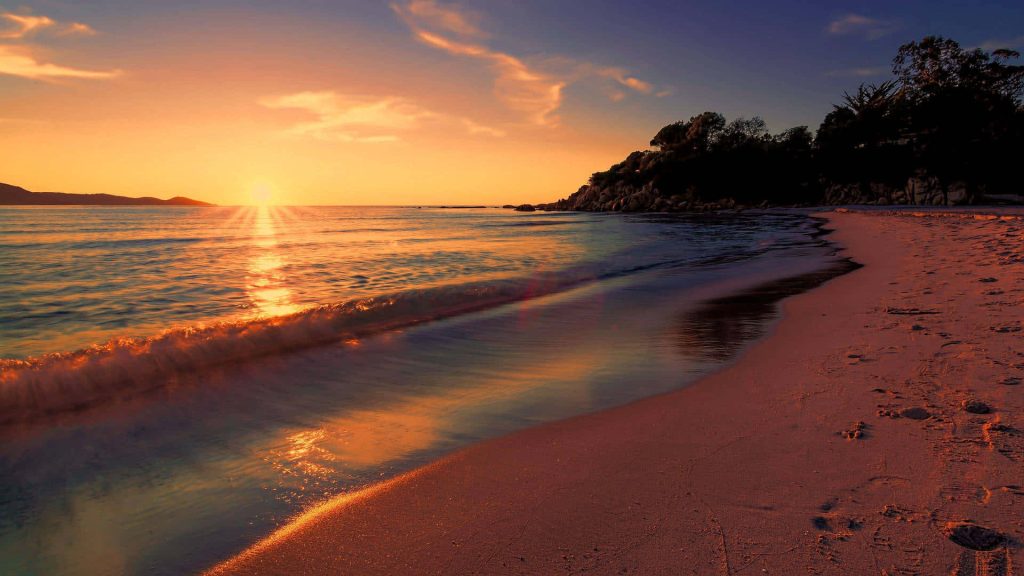 Tranquil beach sunset wallpaper with golden light on surf wet sand and rocky coastline background