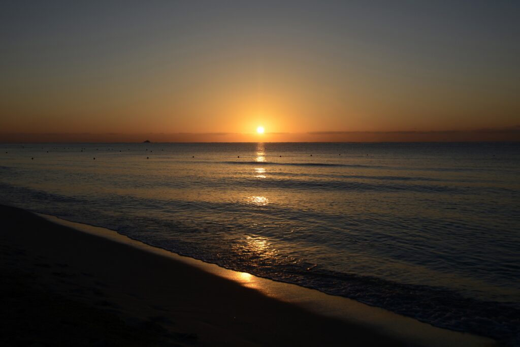 Tranquil beach sunset wallpaper with golden sun reflecting on calm sea and soft orange sky
