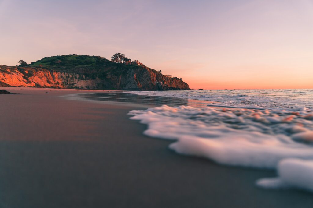 Sunset beach wallpaper with gentle waves soft sea foam rocky shore and lush cliff greenery