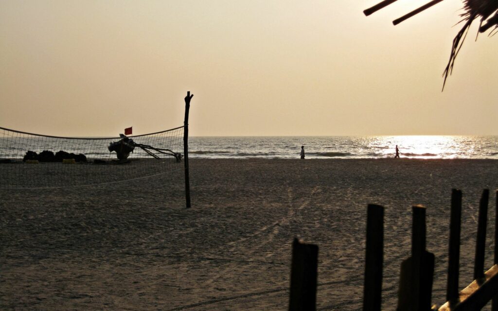 Sunset beach wallpaper with sandy shore volleyball grid calm ocean waves and distant walkers