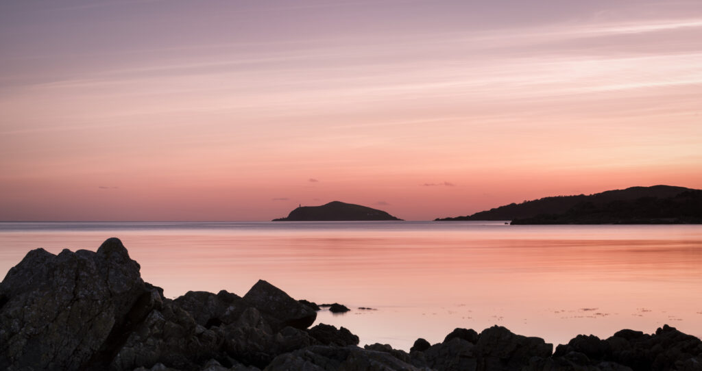 Serene coastline wallpaper with rugged rocks calm sea and distant islands at pink sunset