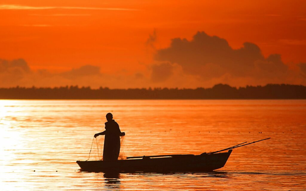 Silhouette of person fishing on boat at sunset with orange sky reflecting on calm water serene scene Wallpaper