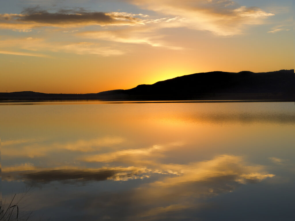 Tranquil sunset wallpaper with dark hill silhouette and warm orange gold reflections on water