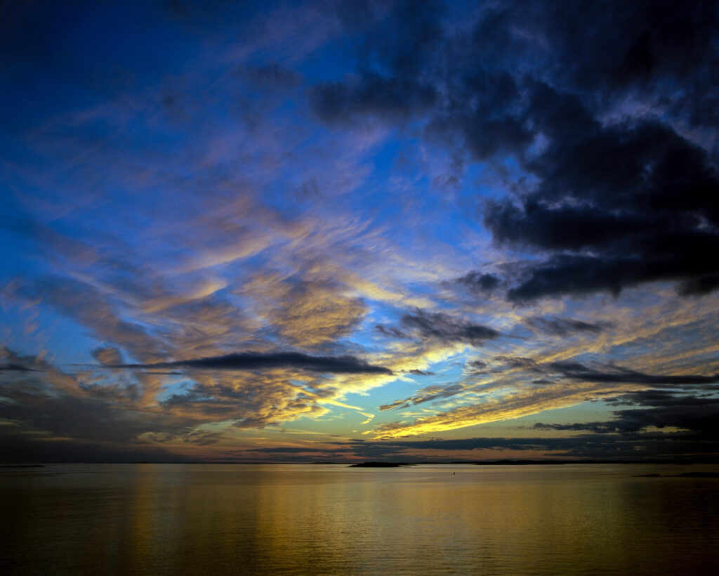 Sunset horizon over calm sea with vivid sky clouds deep blues golds and water reflections wallpaper