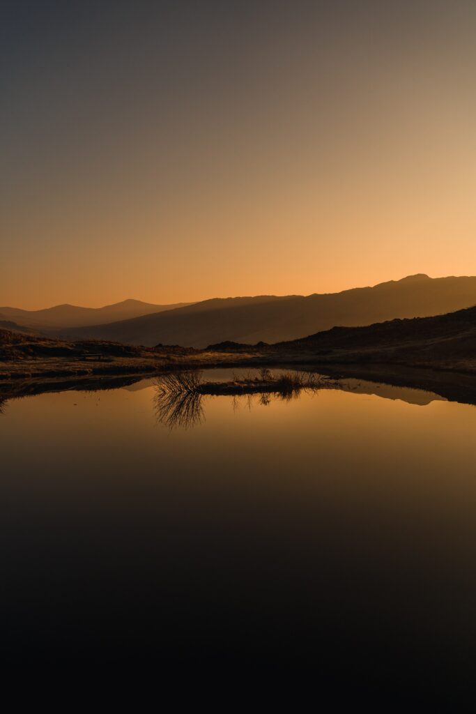 Sunset over peaceful lake reflecting golden light with gentle mountains silhouette wallpaper background