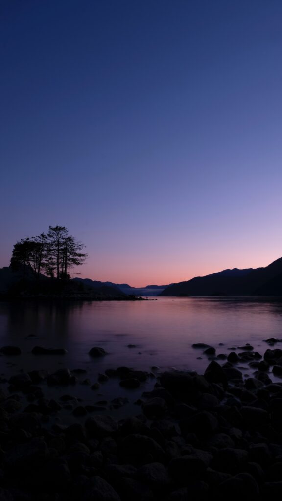 Tranquil lake at sunset reflecting colorful sky with tree and mountain silhouettes peaceful view Wallpaper