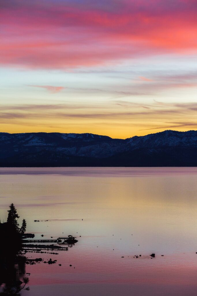 Sunset sky with pink orange purple hues reflecting on tranquil lake near snowcapped mountains Wallpaper