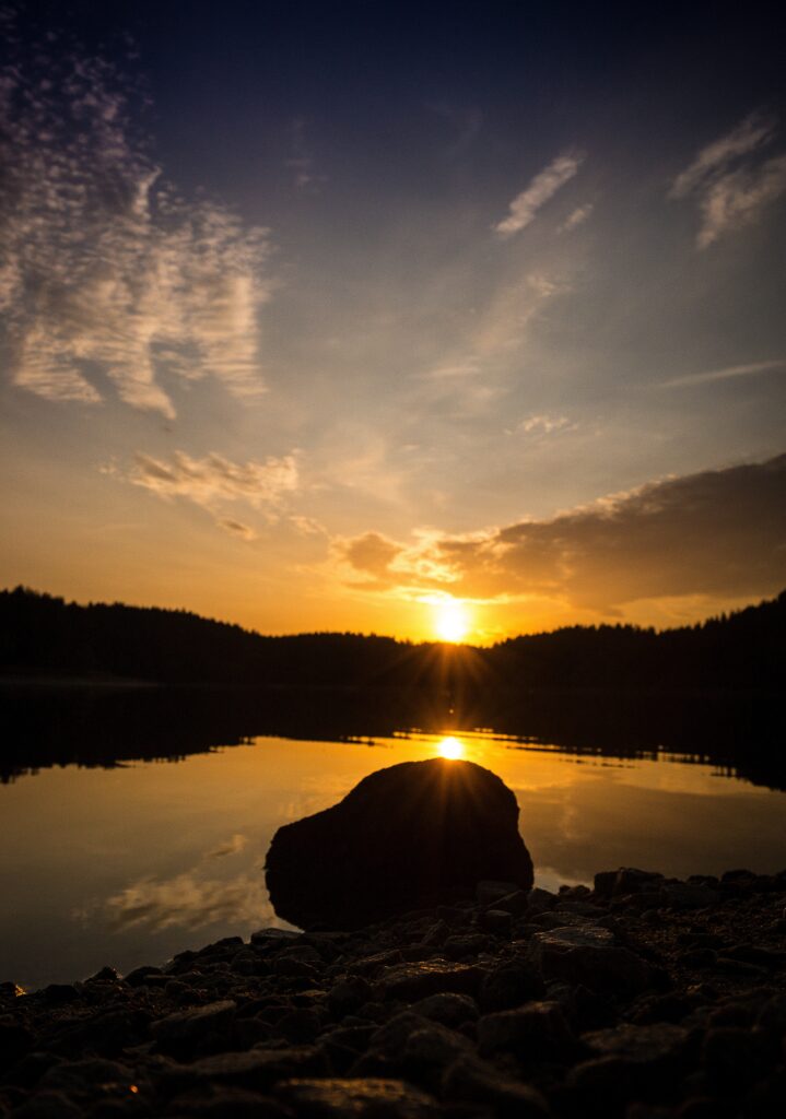 Sunset over tranquil lake with golden sky reflections stones and forest silhouette background Wallpaper