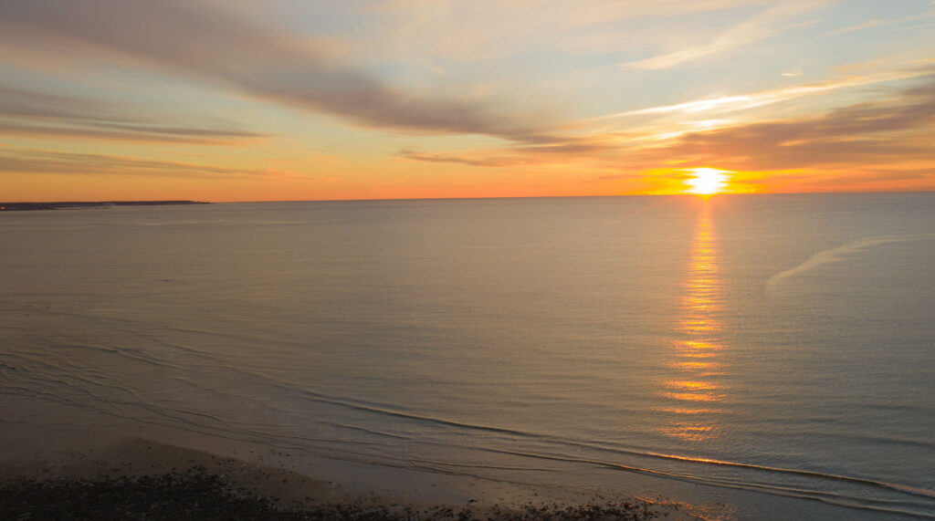 Tranquil sunset over calm sea with golden sunlight reflecting on gentle waves and serene shore Wallpaper