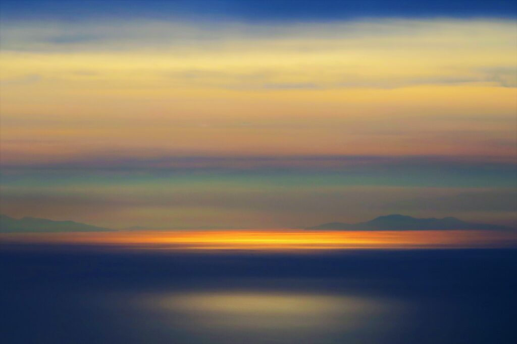 Sunset over calm water with golden light and soft blue orange gradients serene wallpaper background