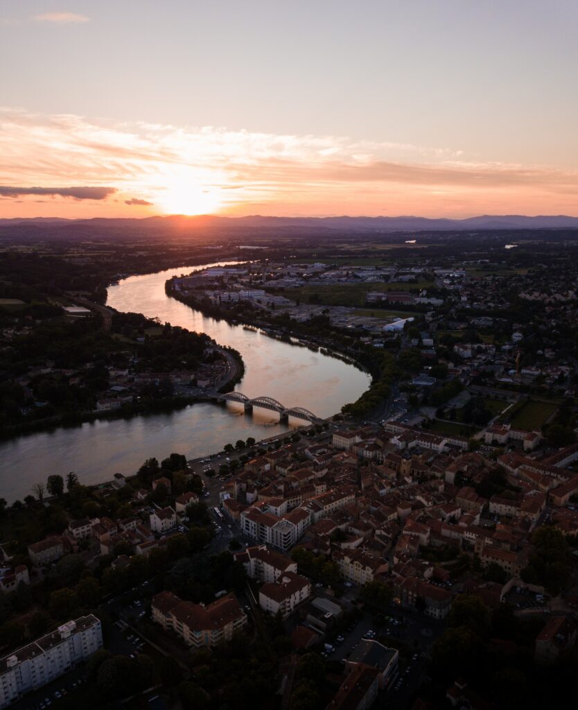 Serene sunset over cityscape with red roofs and river reflecting pastel sky colors wallpaper