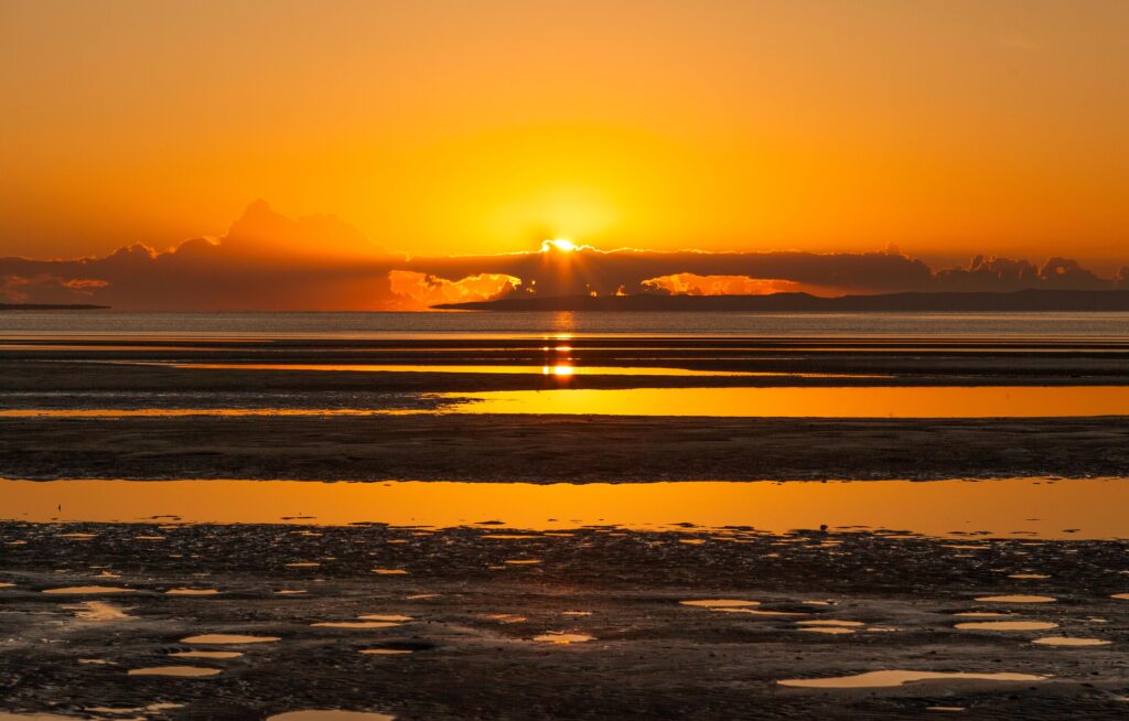 Sunset over calm sea with radiant rays and warm orange glow on reflective shoreline wallpaper