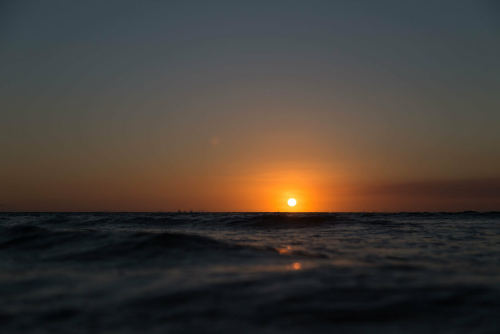 Serene sunset over calm sea with warm orange to deep blue gradient sky wallpaper background