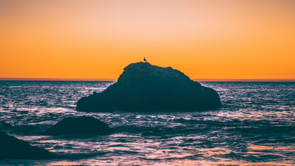 Tranquil sunset over sea with warm orange glow and dark rocks against vibrant coastal sky Wallpaper