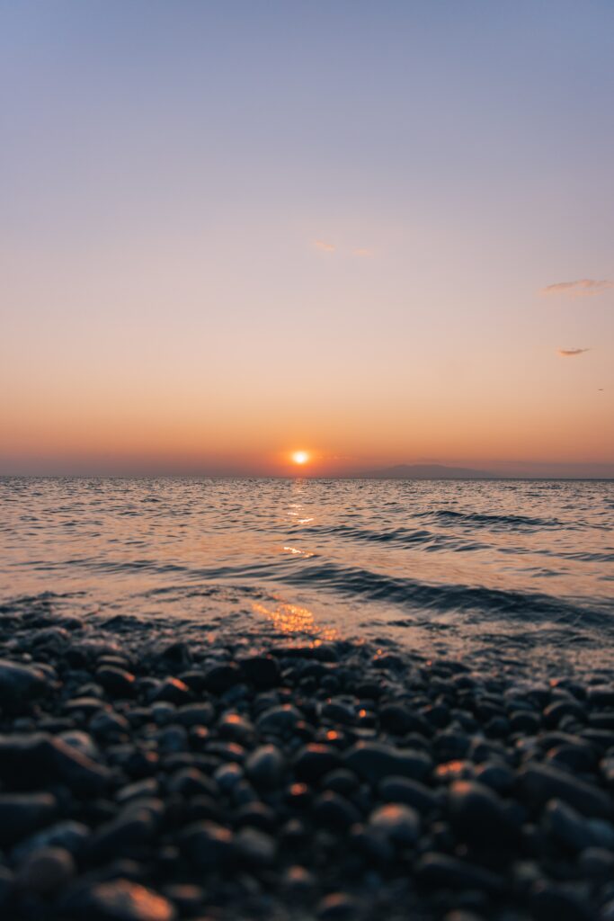 Tranquil sunset over sea with golden light on waves and smooth pebbles on beach wallpaper