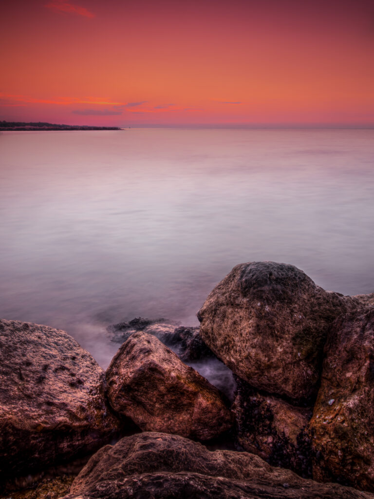 Tranquil sunset coastal wallpaper with textured rocks misty water and vibrant orange purple sky