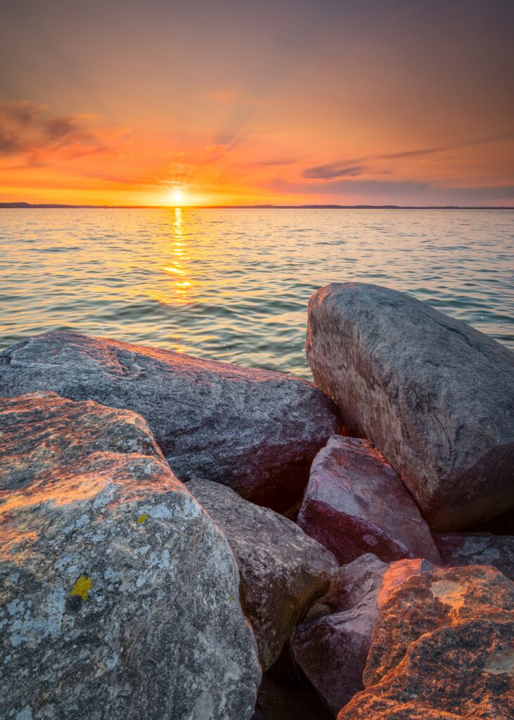 Sunset light on textured sea stones with purple orange sky and gentle waves peaceful scene Wallpaper