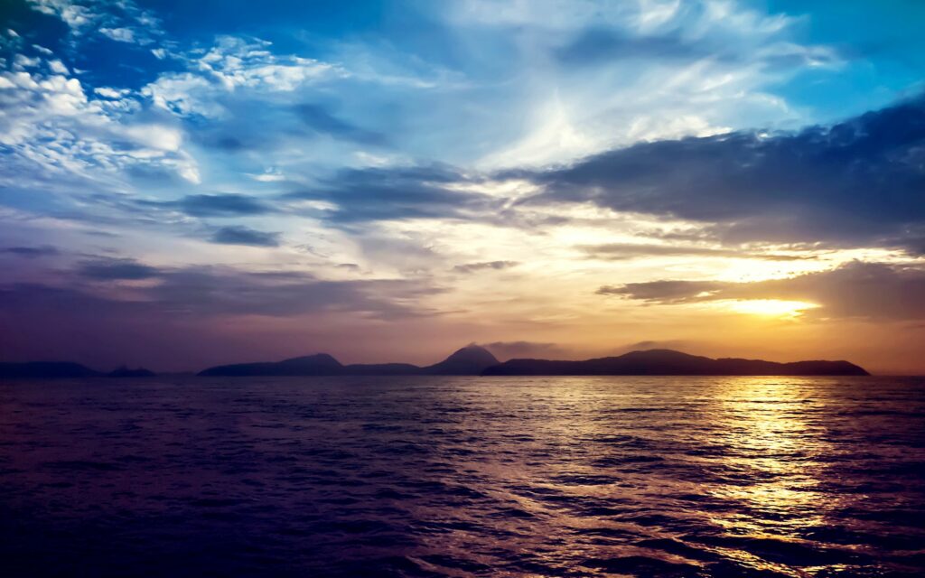 Sunset sea wallpaper with vibrant sky rock formations and calm waves reflecting colorful hues