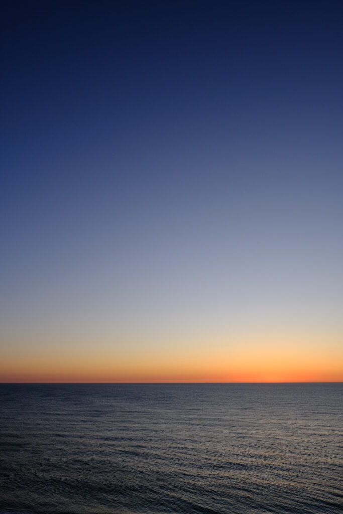 Tranquil sea at sunset with gentle ripples glowing orange horizon and gradient evening sky wallpaper