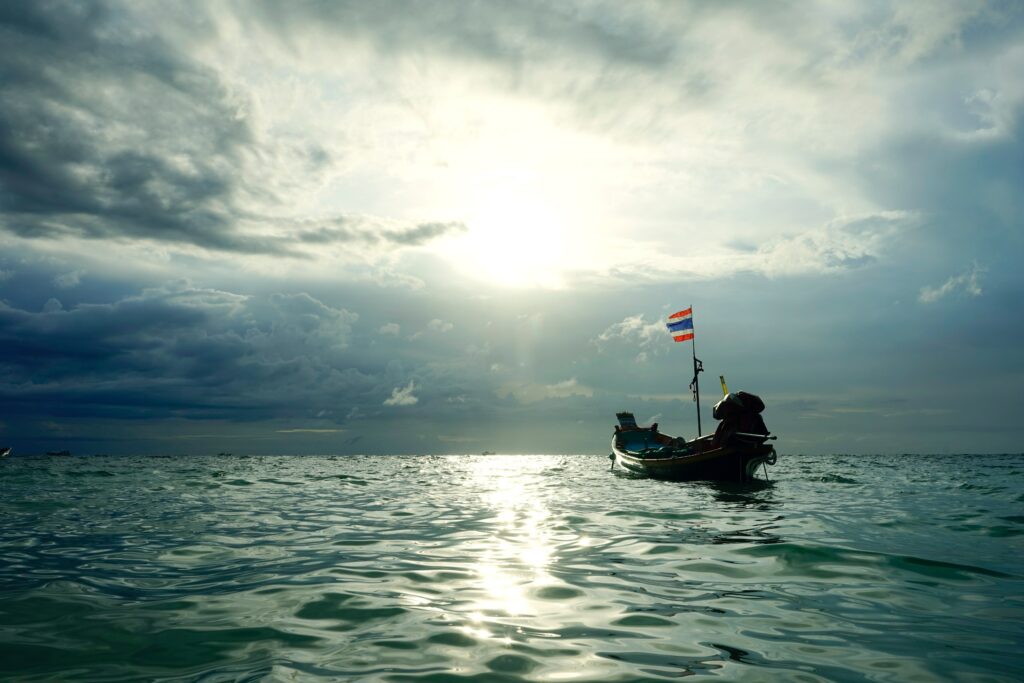 Small boat on shimmering sea at sunset with warm glowing sky and gentle soft waves wallpaper background