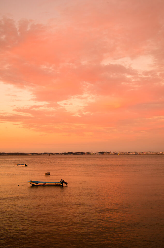Small boats floating on calm sea at sunset with warm orange and pink sky wallpaper background