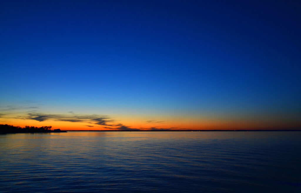 Sunset over calm sea with vivid gradient sky and distant skyline silhouette wallpaper background