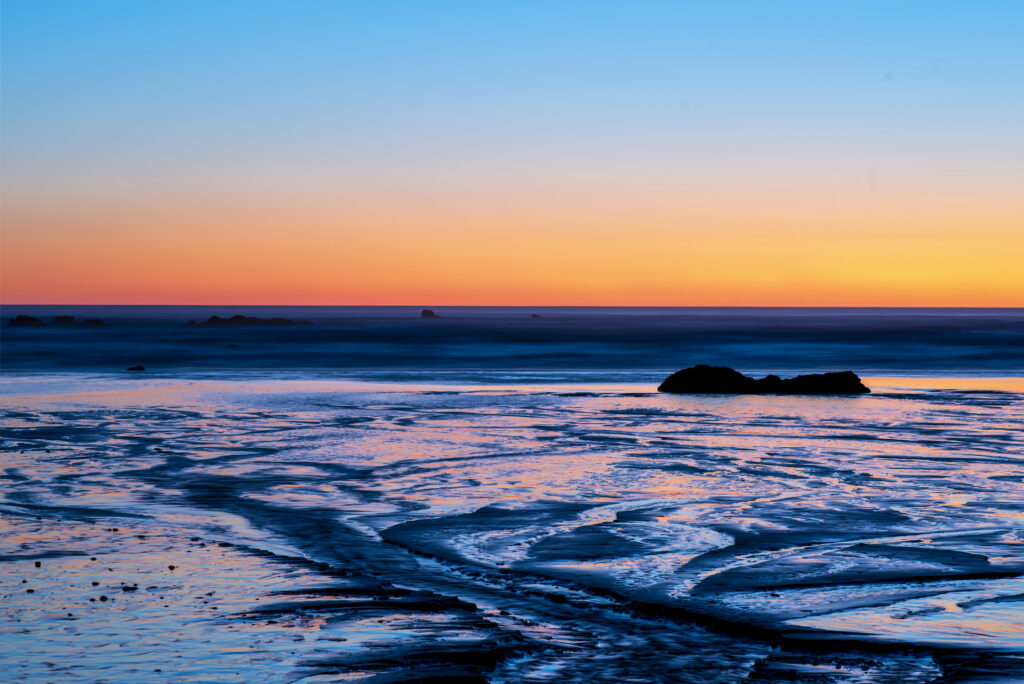 Tranquil sunset sea wallpaper with vivid orange blue hues calm water and dark rocks background