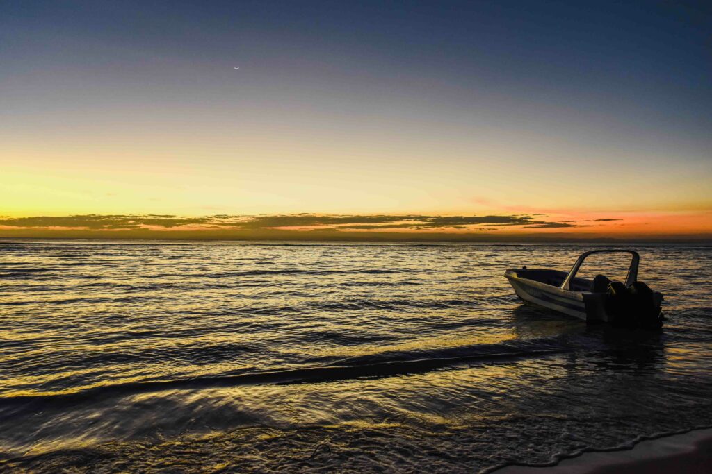 Small boat on rippling sea waves at vivid sunset with deep blue and golden hues wallpaper background