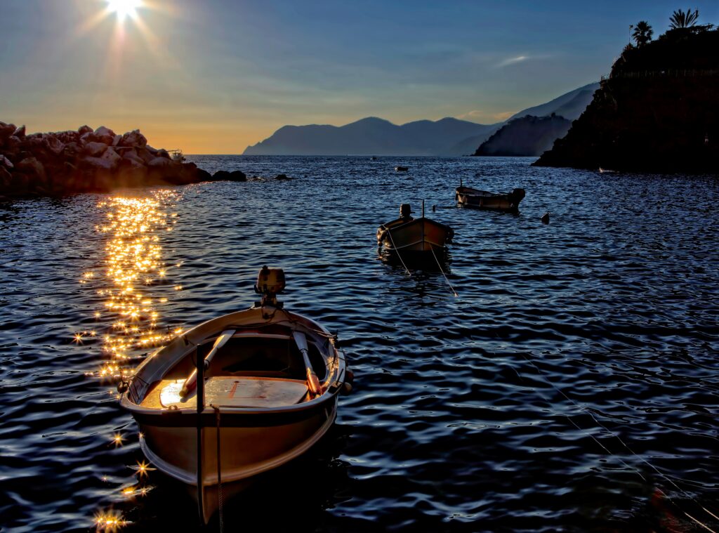 Small boats float on shimmering sea at sunset with golden light and silhouetted mountains Wallpaper