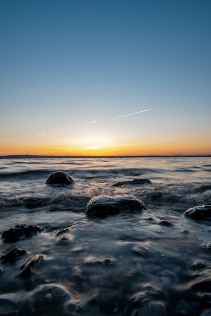 Tranquil sunset seascape with smooth stones and vibrant orange blue sky over calm water Wallpaper