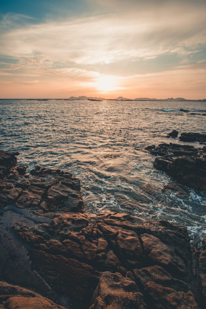 Sunset over calm sea with rugged rocks and soft colorful sky tranquil seascape wallpaper