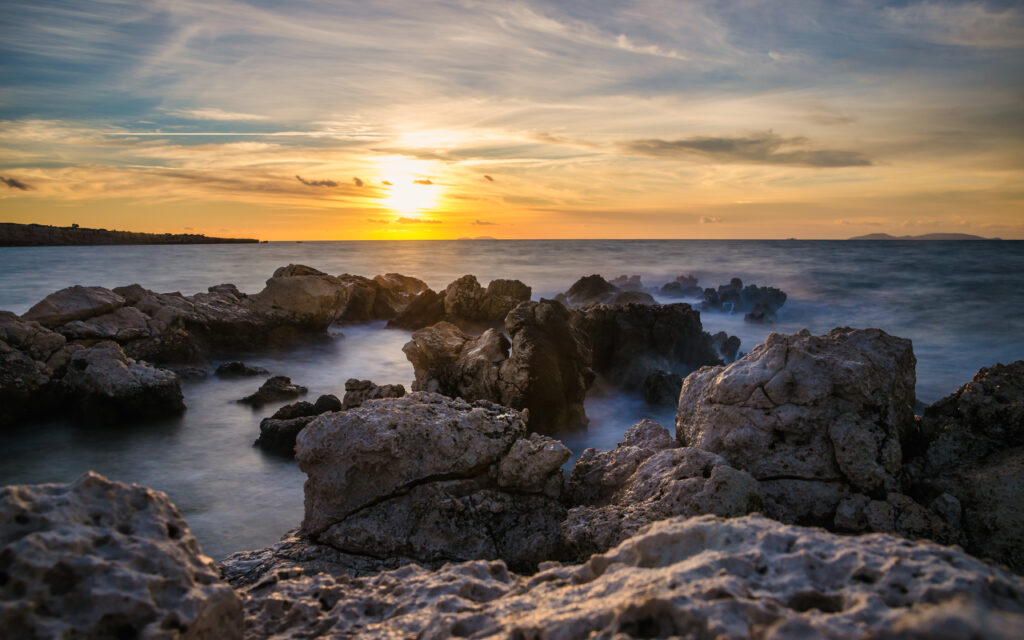 Sunset seascape wallpaper with rugged rocks calm water golden orange sky reflection peaceful view