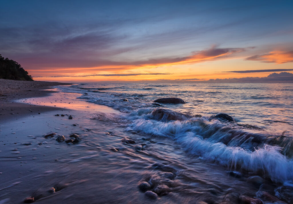 Sunset seaside wallpaper with gentle waves smooth stones warm orange pink purple sky reflection