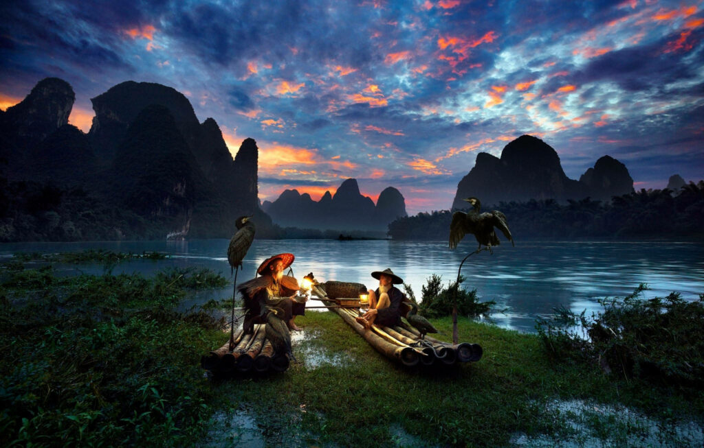 Tranquil Sunset Scene with Bamboo Rafts & Mountain Silhouettes Wallpaper