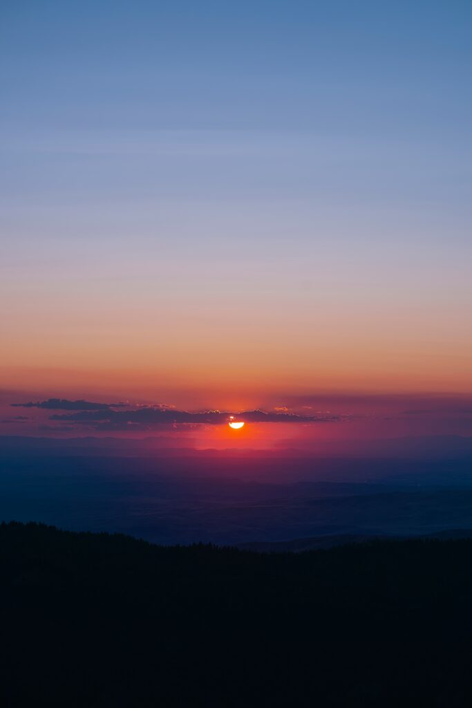 Sunset wallpaper with sun behind clouds casting vibrant orange red and purple hues across sky