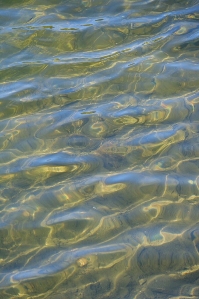 Transparent sea water with sunlit sandy bottom and shimmering blue golden ripples wallpaper