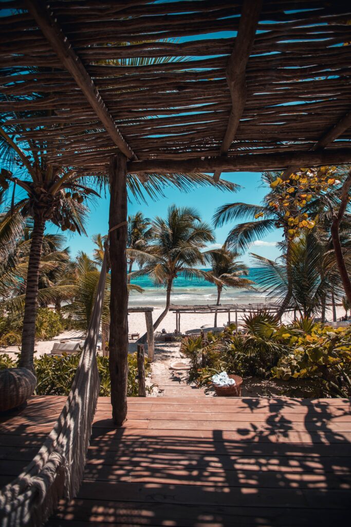 Tropical beach view with palm trees lush greenery and ocean seen from rustic wooden veranda Wallpaper