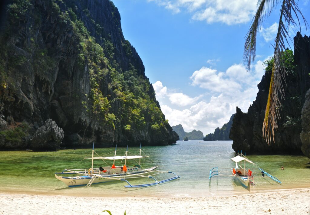 Crystal-clear tropical beach with traditional boats limestone cliffs and vibrant blue sky paradise Wallpaper