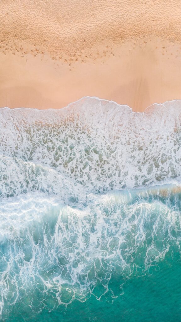 Aerial view of tranquil beach with turquoise waves gently meeting soft sandy shores wallpaper