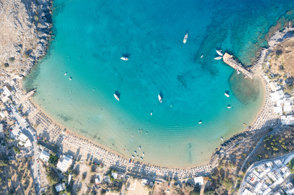 Aerial view of turquoise sea coastal village sandy beach anchored boats cliffs bright sunlight Wallpaper