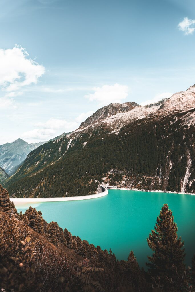 Turquoise lake surrounded by steep mountains and dense green forests under a clear sky wallpaper