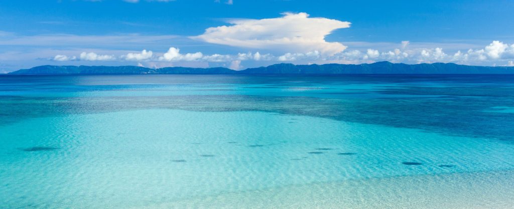 Widescreen wallpaper of crystal-clear turquoise ocean with tropical mountains and blue sky