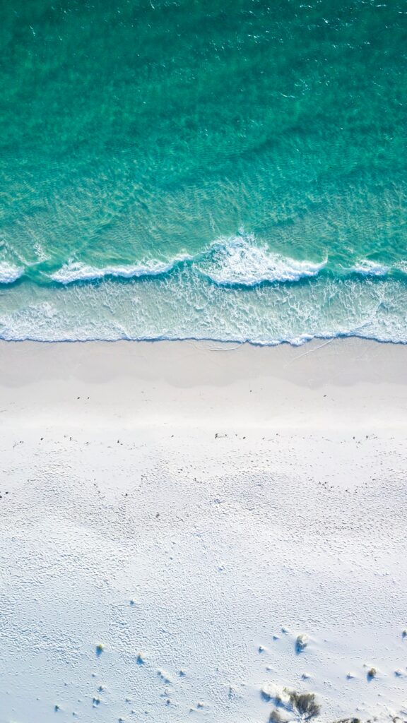 Aerial view of turquoise ocean waves gently meeting pristine white sandy beach high resolution Wallpaper