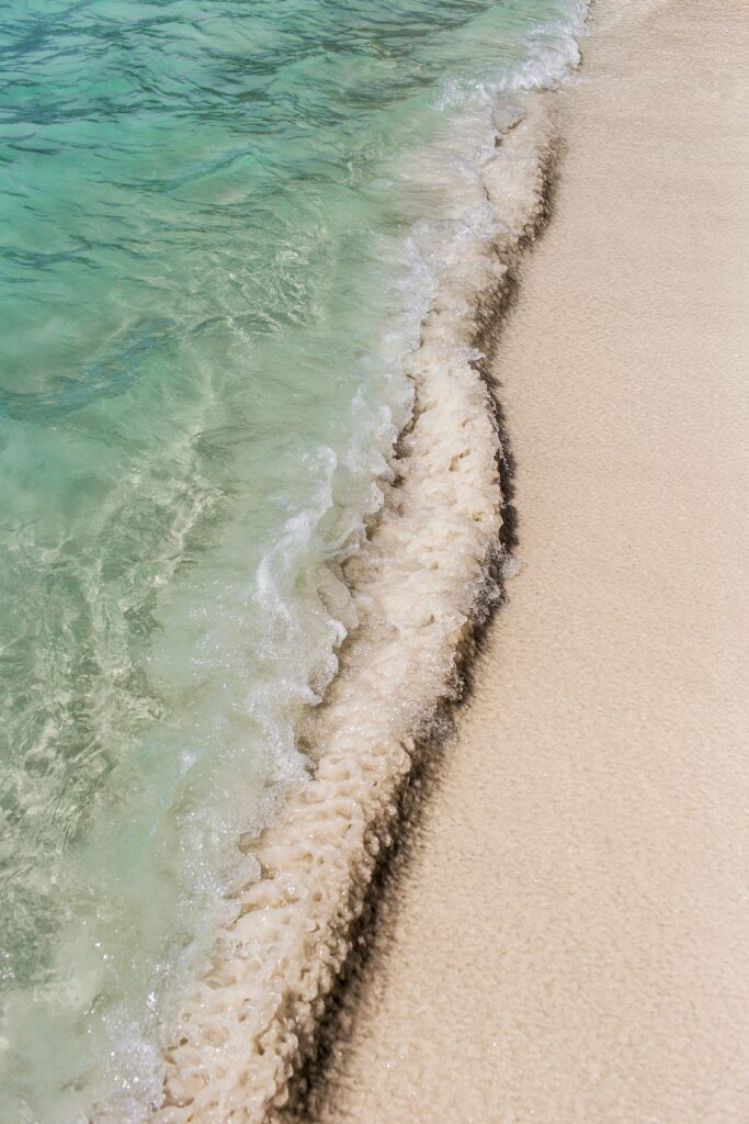 Gentle wave washes soft beige sand with clear turquoise sea in a tranquil beach setting wallpaper
