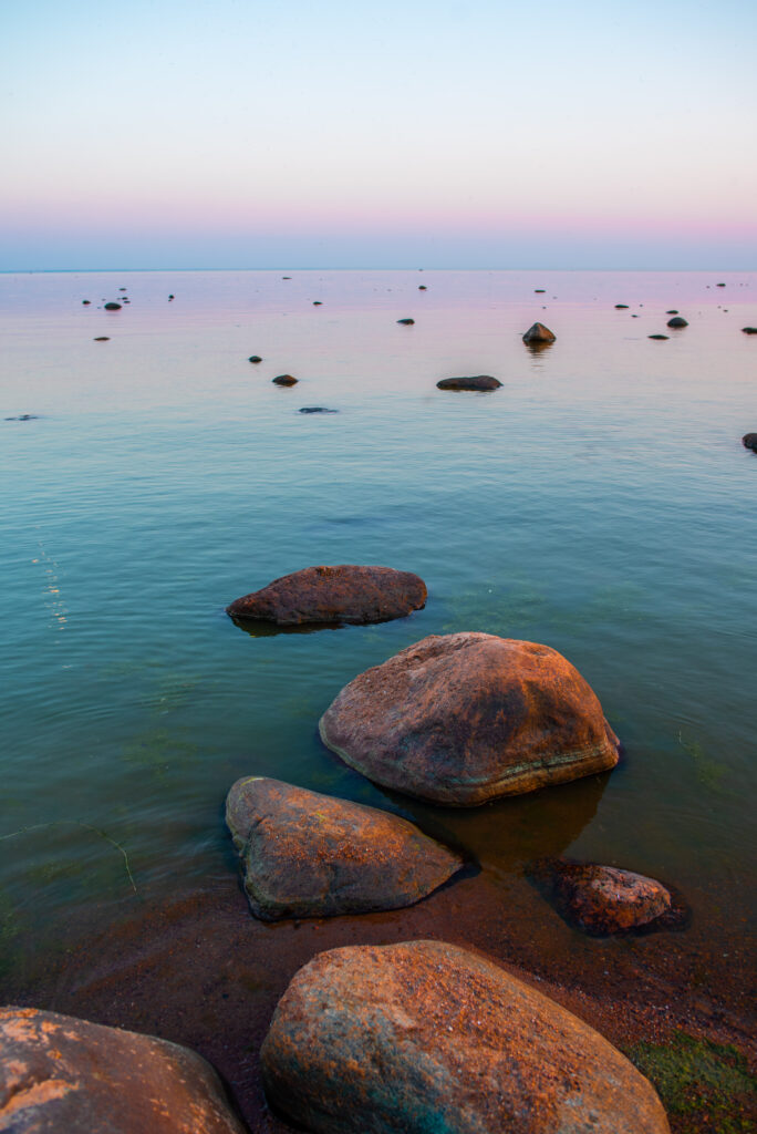 Tranquil coastal twilight with smooth stones and pastel pink blue purple calm sea waters wallpaper