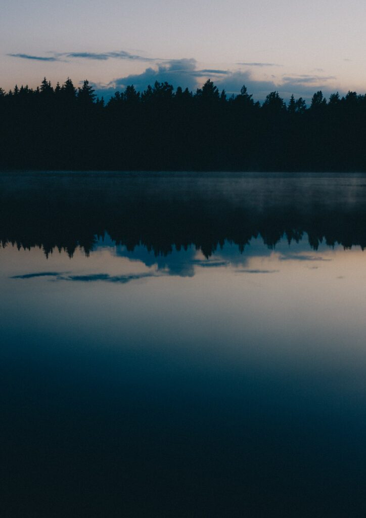 Tranquil twilight forest silhouette with soft clouds reflected on calm lake peaceful wallpaper