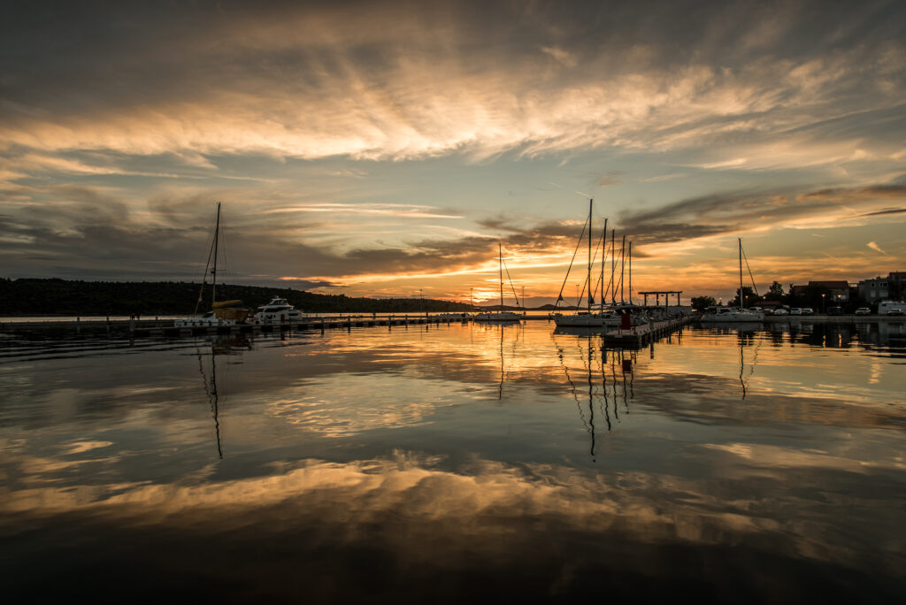 Tranquil twilight lake with boats docked by pier reflecting warm sunset colors and calm water Wallpaper