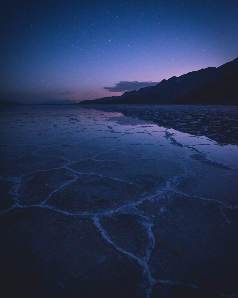 Tranquil twilight lake with rugged mountain silhouettes and starry deep blue purple sky wallpaper