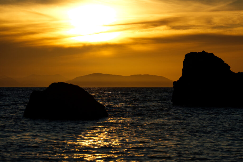 Tranquil twilight sea with rugged rocks golden sunset sky and distant mountains wallpaper background